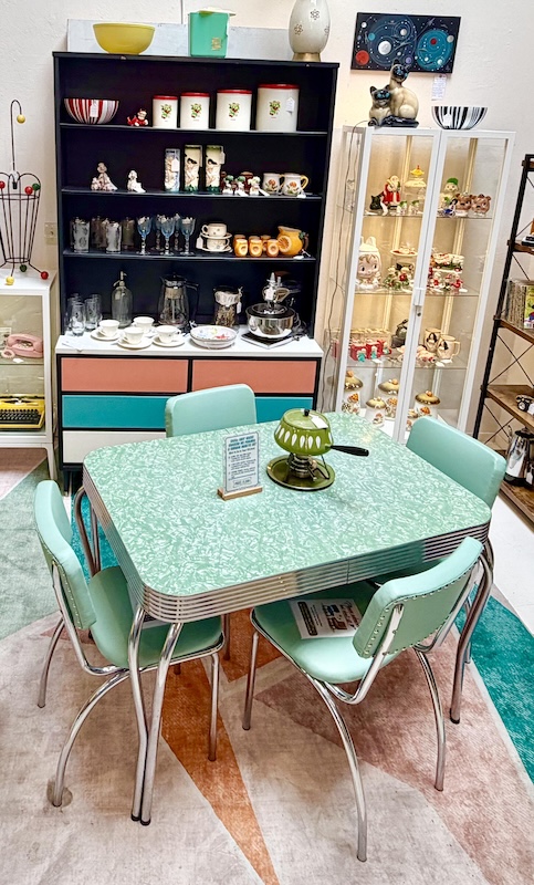A vintage 1950s mint green 'cracked ice' Formica kitchen table with triple-ribbed chrome edging and four matching mint green vinyl upholstered chairs with chrome legs, displayed in an antique booth at Antique Society in Sebastopol