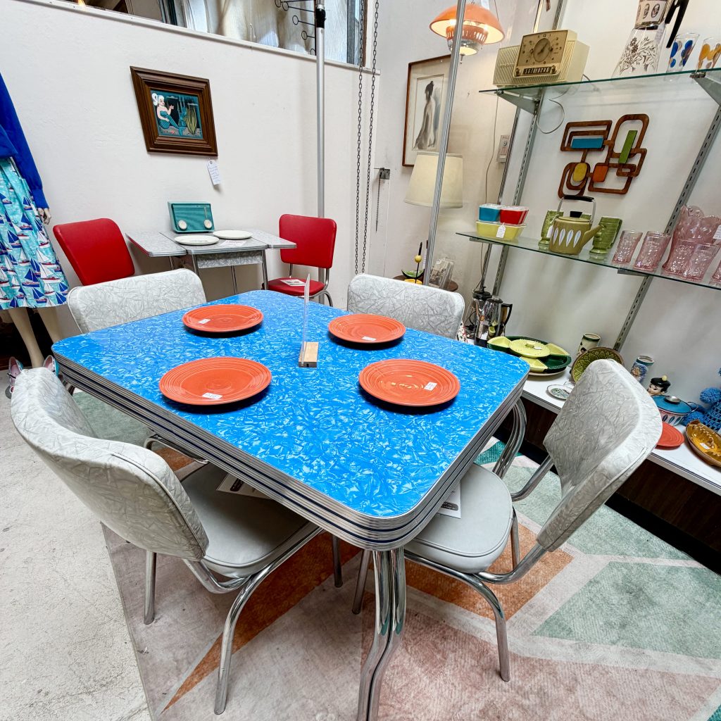 A vintage 1950s blue 'cracked ice' Formica kitchen table with triple-ribbed chrome edging and four matching vinyl upholstered chairs with chrome legs, displayed in an antique booth at Antique Society in Sebastopol